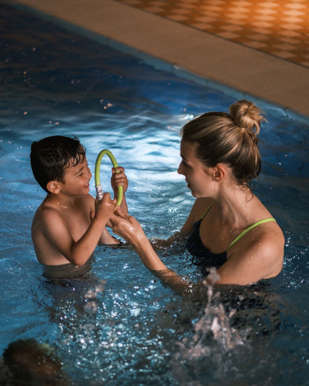 Schwimmtrainerin übt mit einem Kind spielerisch im Wasser