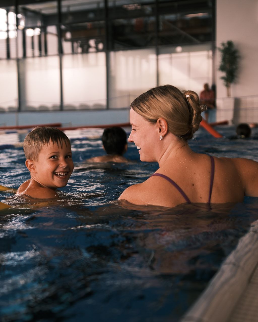 Kind schwimmt lachend neben seiner Trainerin im Schwimmkurs