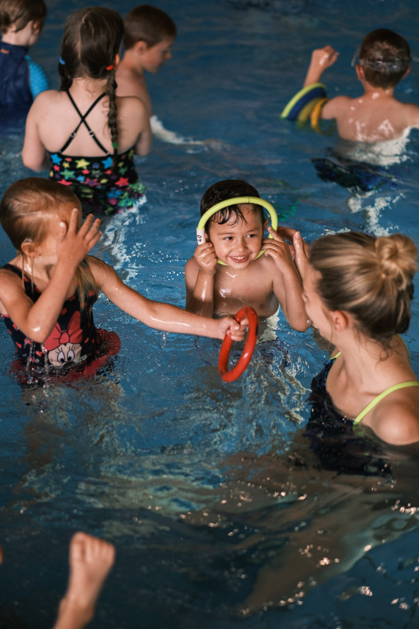 Kinder lernen spielerisch mit Schwimmnudeln in einer kleinen Schwimmgruppe