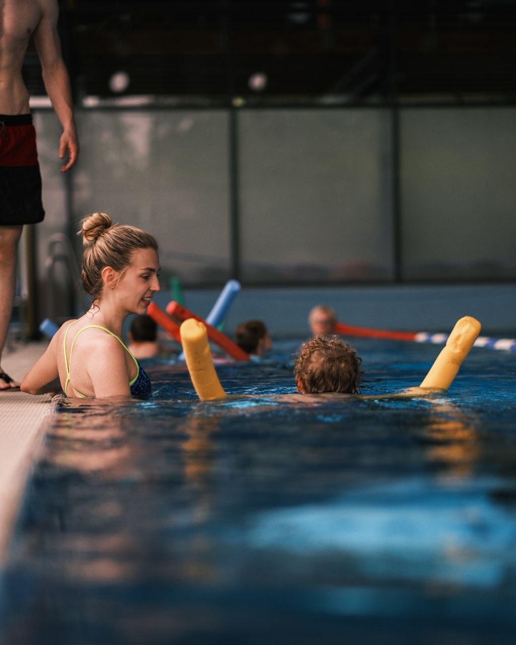Schwimmtrainerin begleitet ein Kind aufmerksam beim Üben mit der Schwimmnudel